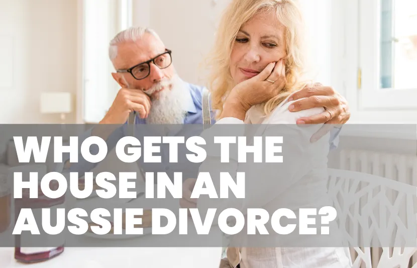 Older man with a white beard and glasses sitting at a table, looking at a woman who appears upset and distant. The woman rests her face on her hand, looking away. White overlay text reads “Who Gets the House in an Aussie Divorce?